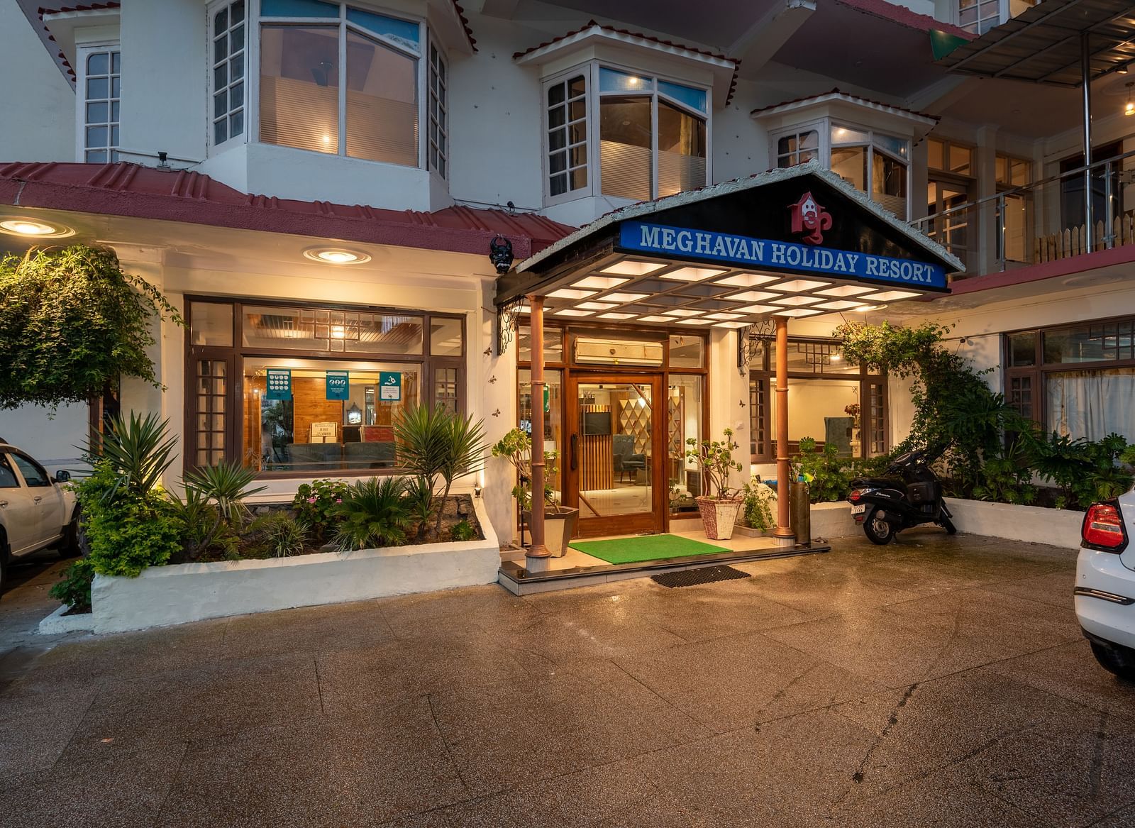 A photo of the entrance to DLS Meghavan Resort, showing the building's facade, entrance way, and some potted plants.